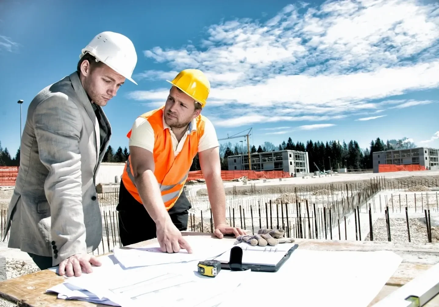 Two men in hard hats looking at plans on a table.