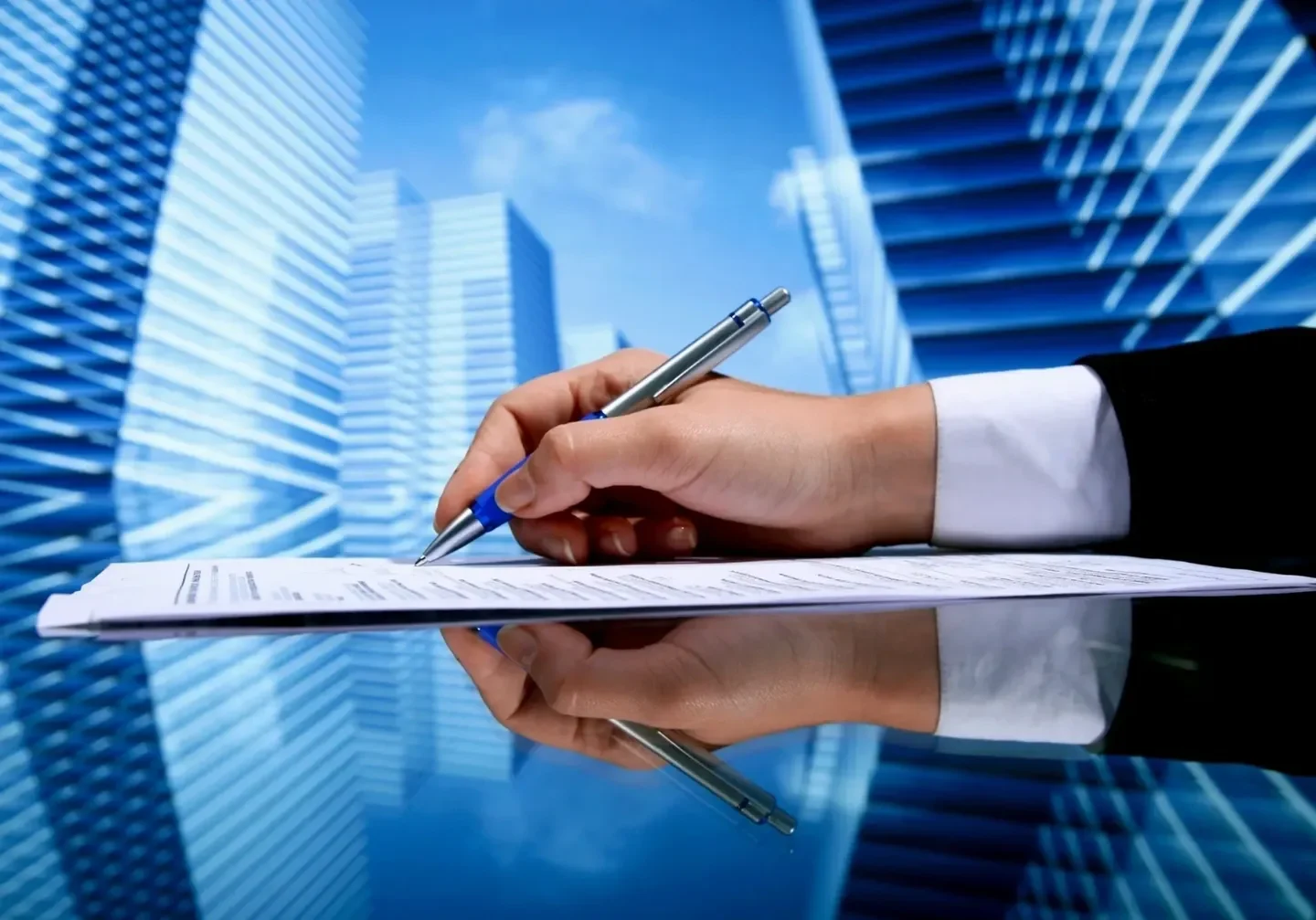 A person writing on paper with buildings in the background.