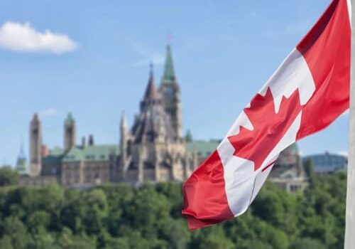 A canadian flag flying in front of the parliament building.